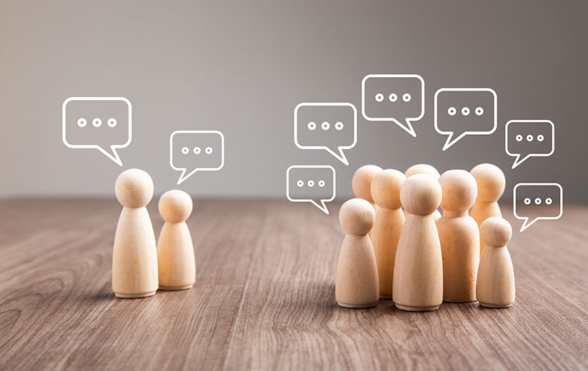 Mehrere Holzfiguren mit Sprechblasen in einer Diskussion