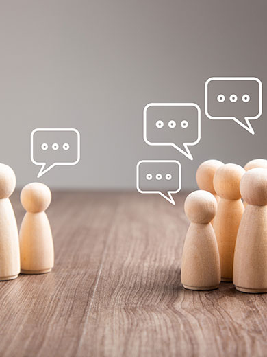 Mehrere Holzfiguren mit Sprechblasen in einer Diskussion