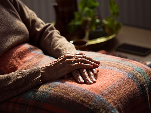 Ältere Person liegt mit gefalteten Händen unter einer Decke.