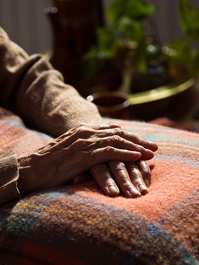 Ältere Person liegt mit gefalteten Händen unter einer Decke.